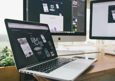 Ordinateur portable et écrans affichant des maquettes graphiques sur un bureau en bois
