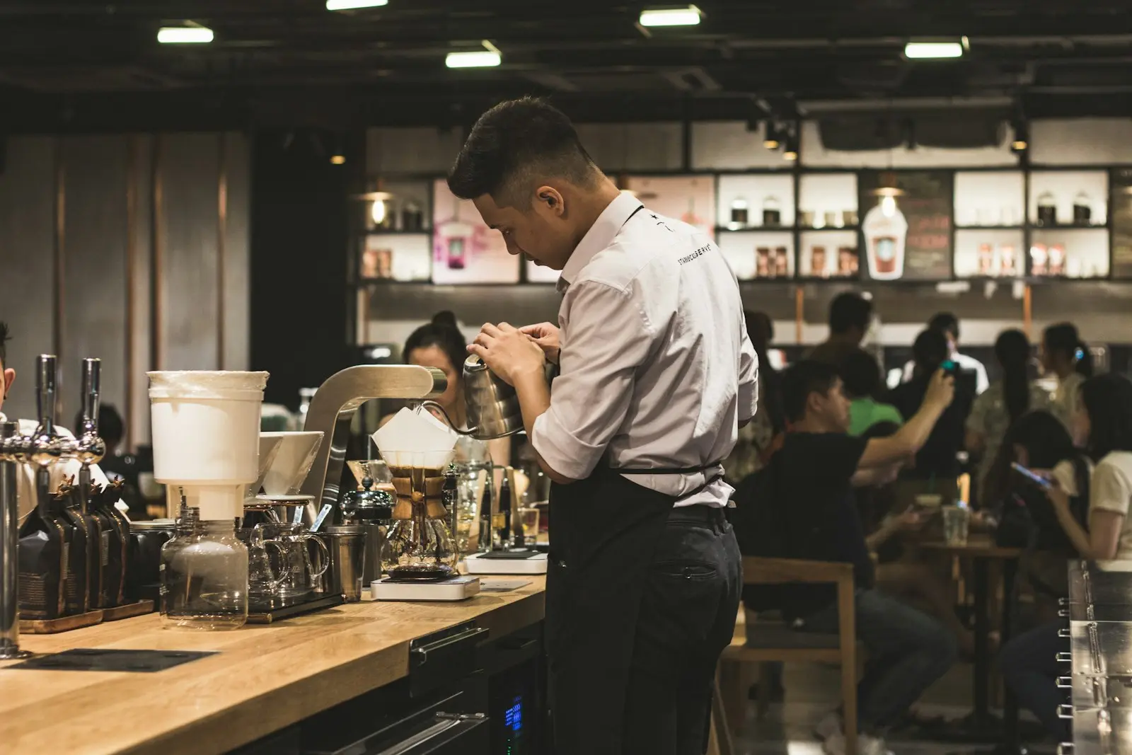 Barista préparant un café filtre au comptoir d'un café animé et fréquenté