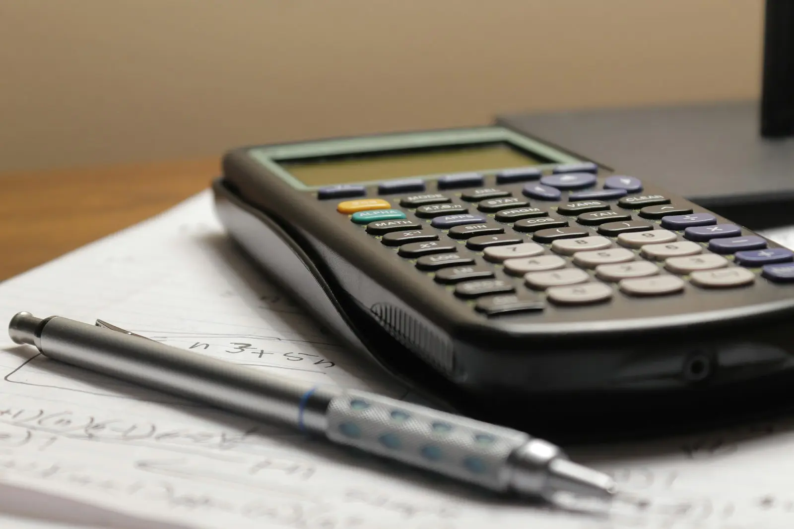 Gros plan sur une calculatrice scientifique posée sur des notes de calculs manuscrites