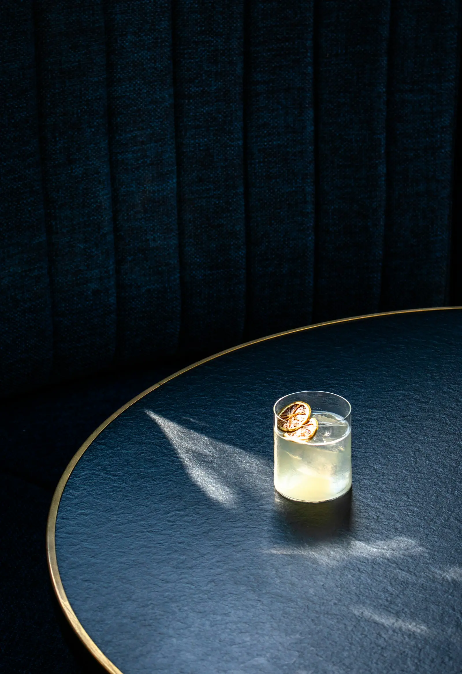 Verre de cocktail garni de rondelles d'agrumes séchées posé sur une table ronde dans un bar tamisé