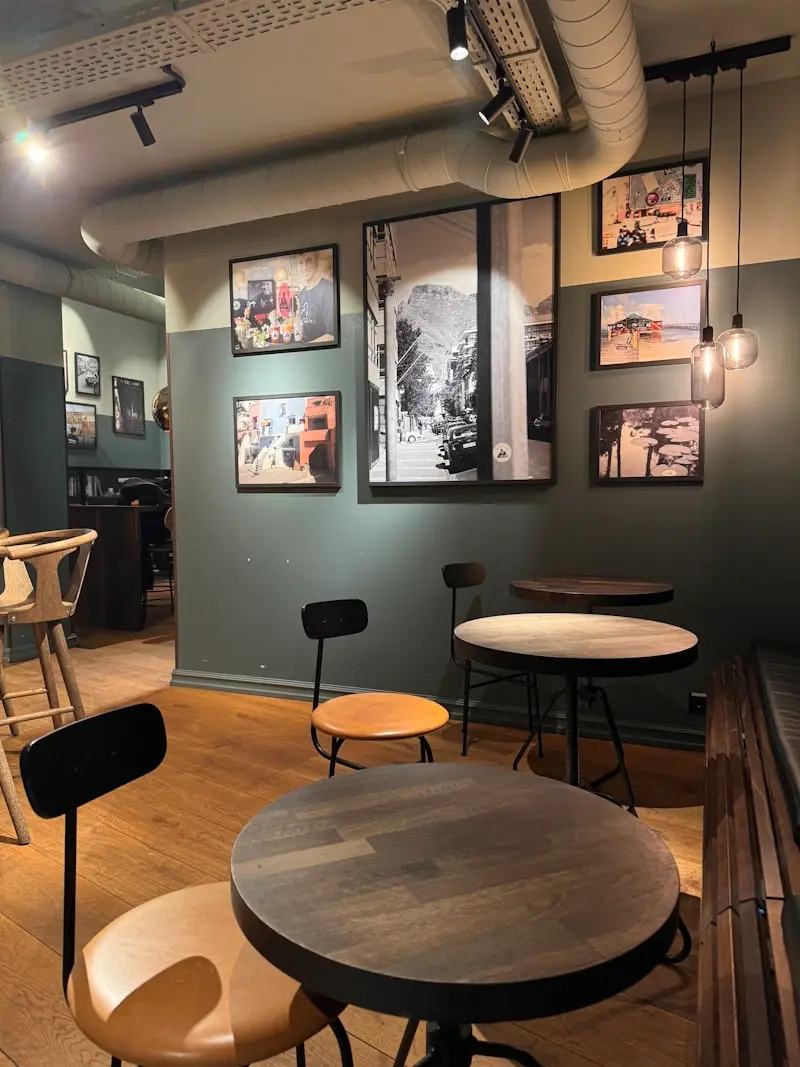 Salle de bistrot avec tables rondes en bois, tabourets en cuir et cadres photo au mur