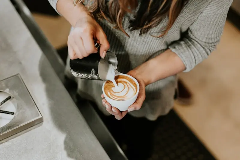 Barista versant du lait pour réaliser un latte art sur un cappuccino