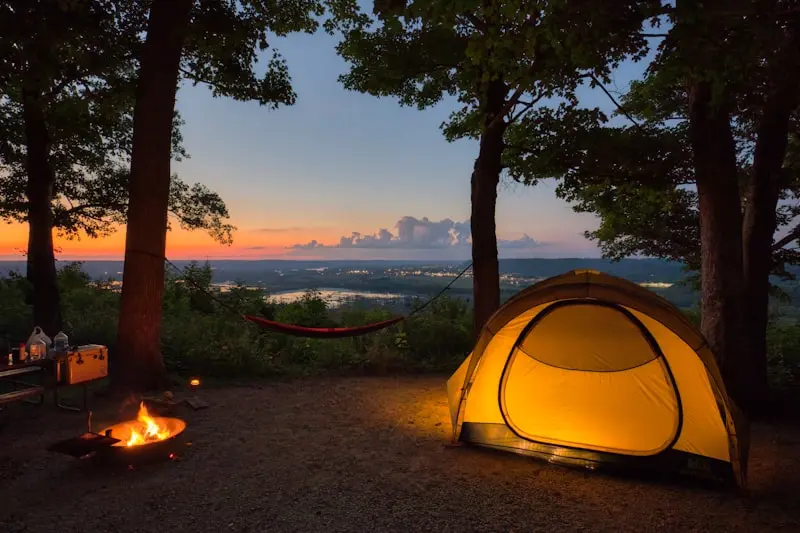 Tente de camping illuminée au crépuscule avec vue panoramique, visuel pour création site internet camping