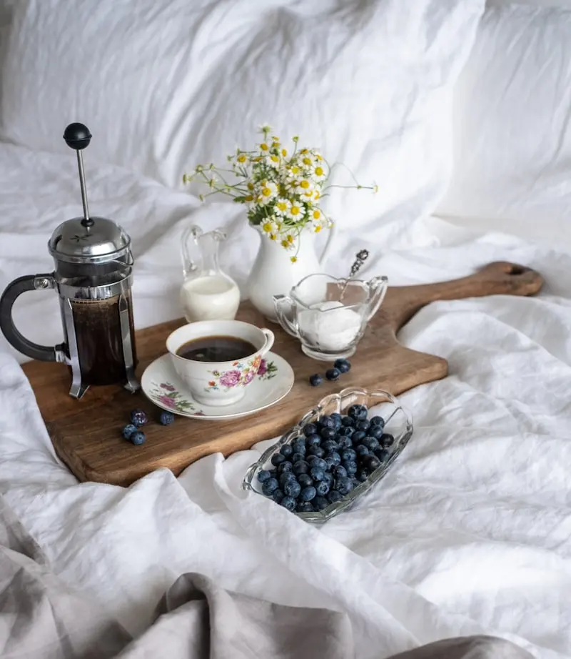 Plateau petit-déjeuner raffiné sur lit avec cafetière, fleurs et myrtilles, exemple site internet chambre d'hôtes