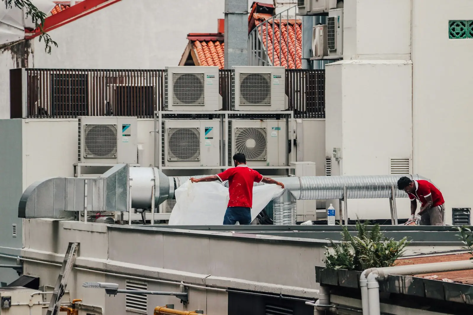 Techniciens chauffagistes intervenant sur des unités de climatisation en toiture d'immeuble