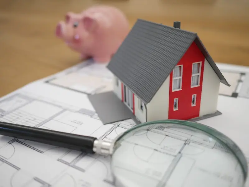 Maquette de maison, loupe et tirelire sur un plan, représentant l'expertise immobilière