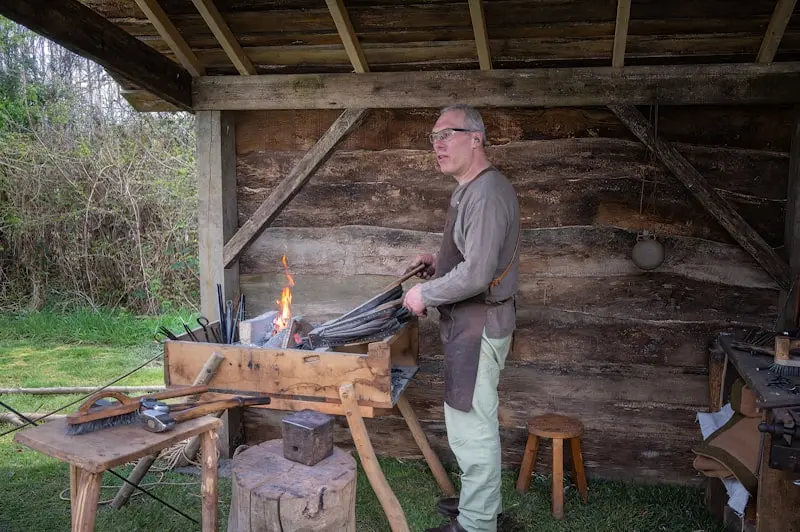 Ferronnier d'art chauffant une pièce de métal dans une forge extérieure, création de site pour artisan