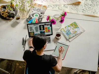 Illustrateur travaillant sur un ordinateur portable entouré de dessins, fleurs et carnets, création site internet créatif