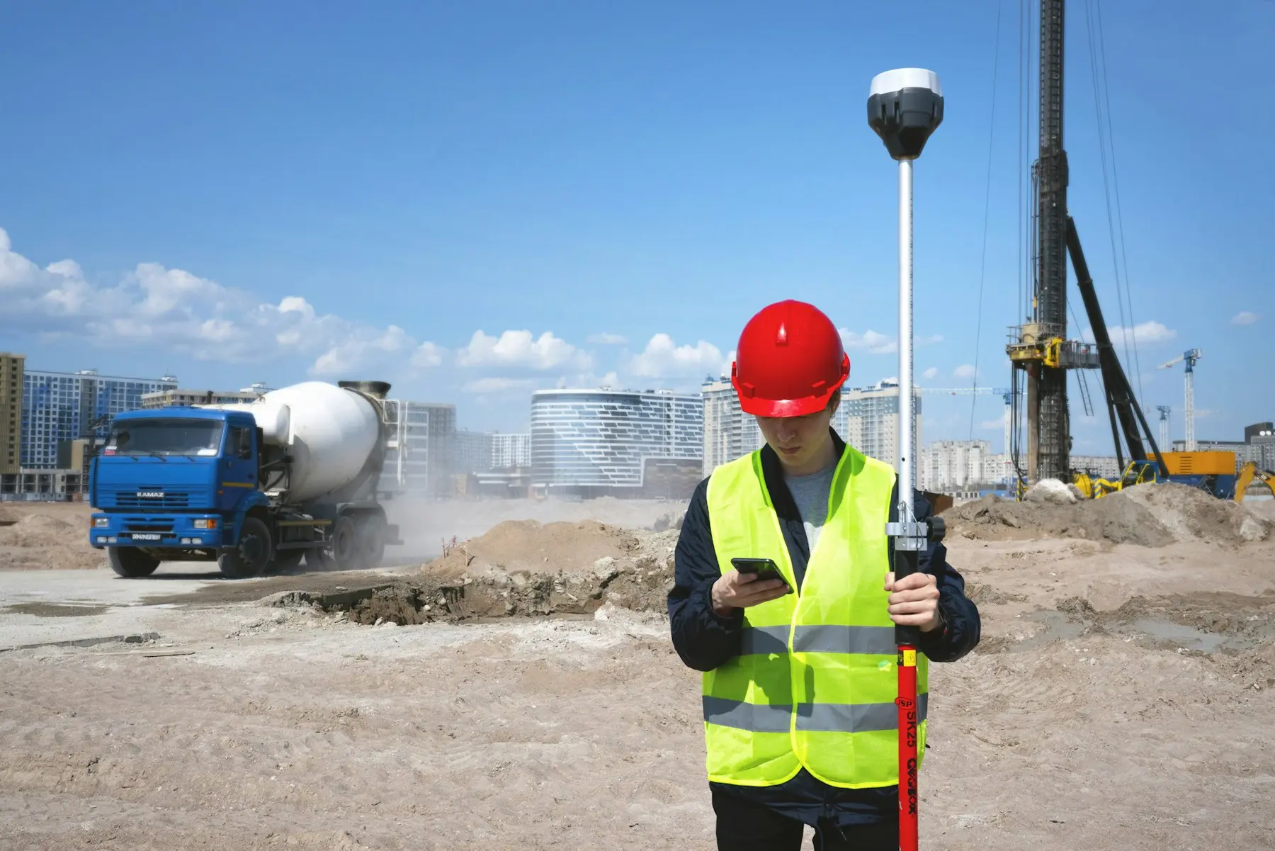Géomètre avec casque rouge et GPS de chantier vérifiant les données sur smartphone