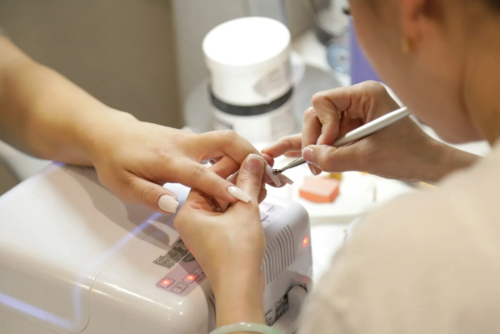 Prothésiste ongulaire réalisant une pose d'ongles avec lampe UV - création site internet nail art