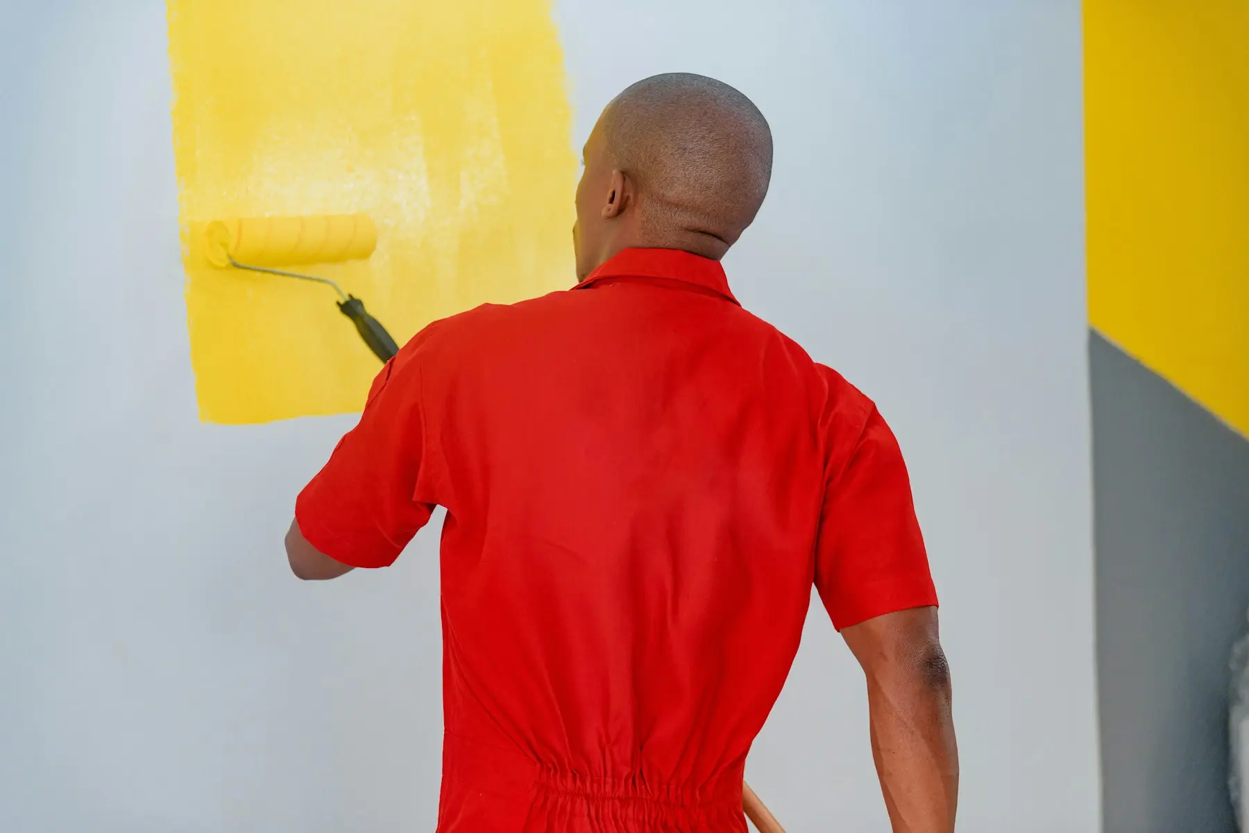 Peintre appliquant une peinture jaune au rouleau sur un mur en cours de finition