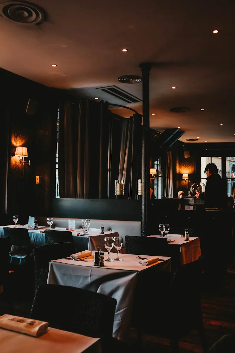 Salle de restaurant gastronomique feutrée avec tables dressées, rideaux et éclairage tamisé