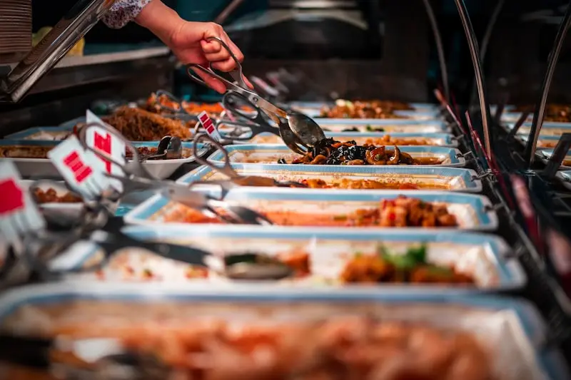 Buffet de traiteur avec plats variés dans des bacs inox et pince de service en action