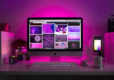 Écran d'ordinateur iMac affichant une galerie photo sous un éclairage d'ambiance rose