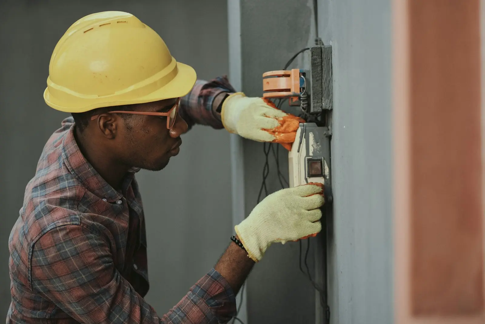 Électricien en casque de chantier raccordant un boîtier électrique mural sur site