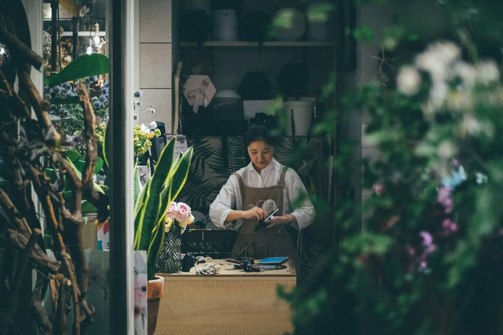 Fleuriste concentrée en train de composer un bouquet dans son atelier entouré de plantes