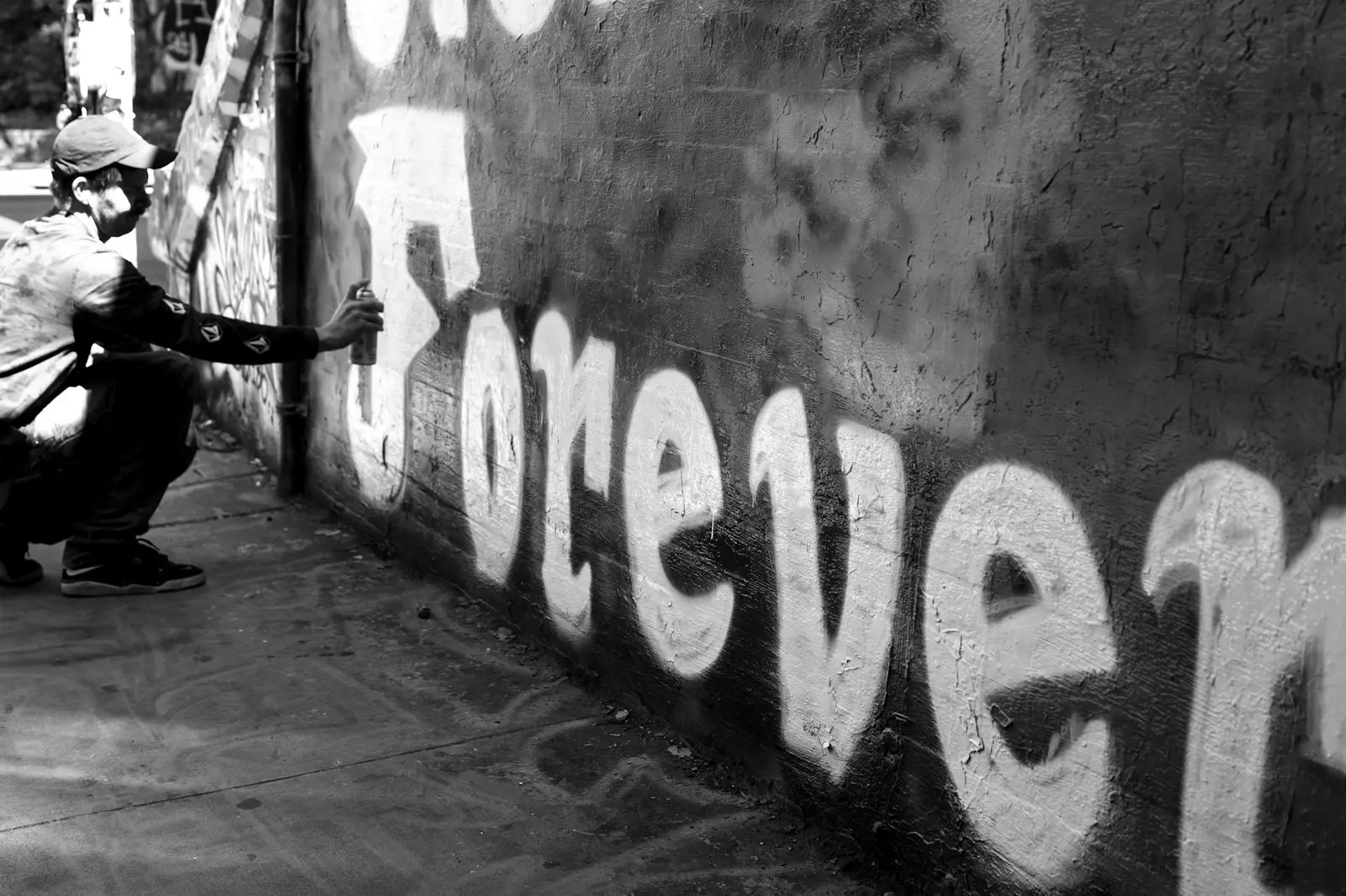 Graffeur agenouillé traçant en noir et blanc le mot "forever" sur un mur de rue
