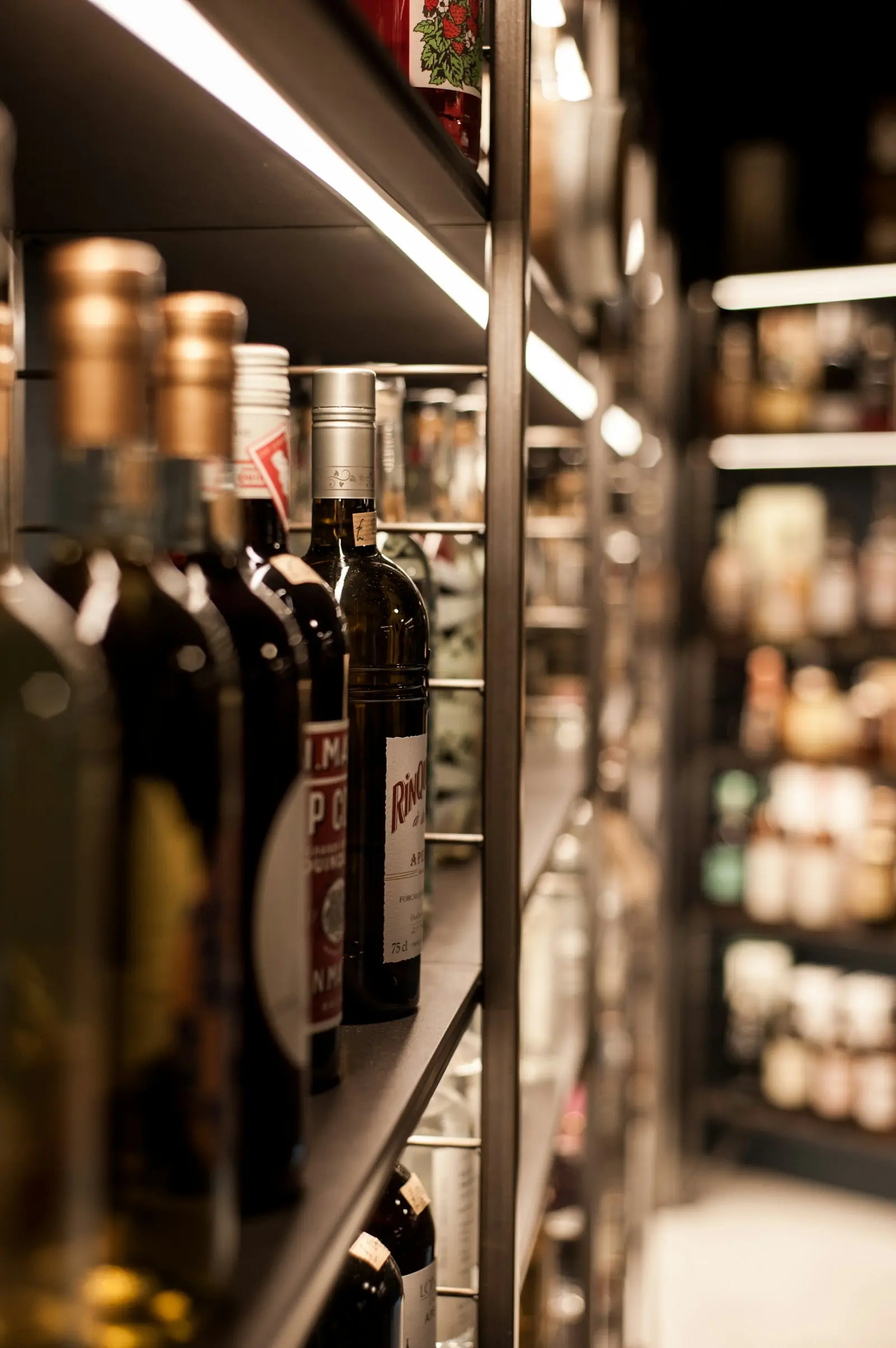 Gros plan sur des bouteilles de vin alignées, capsules dorées et argentées en cave à vin