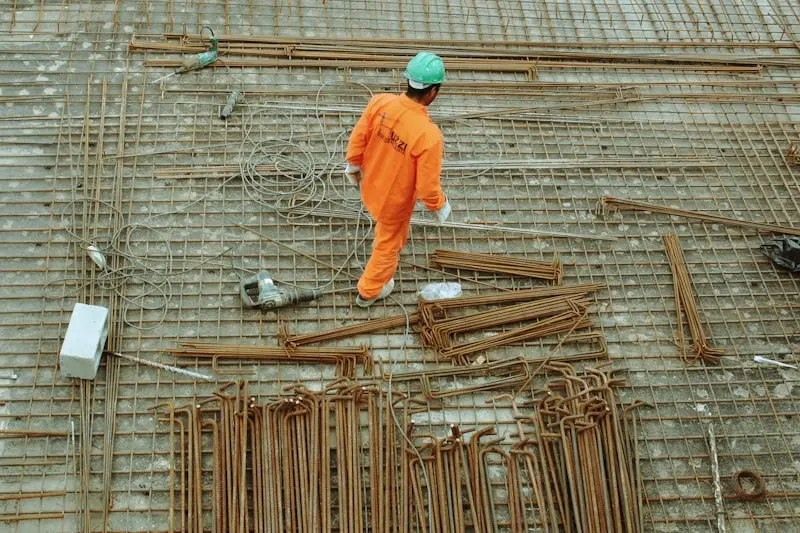 Maçon en combinaison orange posant un ferraillage d'armature sur une dalle en construction