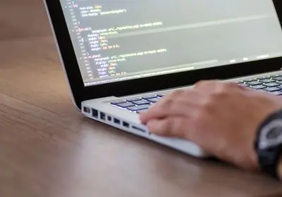 Mains tapant du code sur un clavier d'ordinateur portable, lignes de programmation à l'écran
