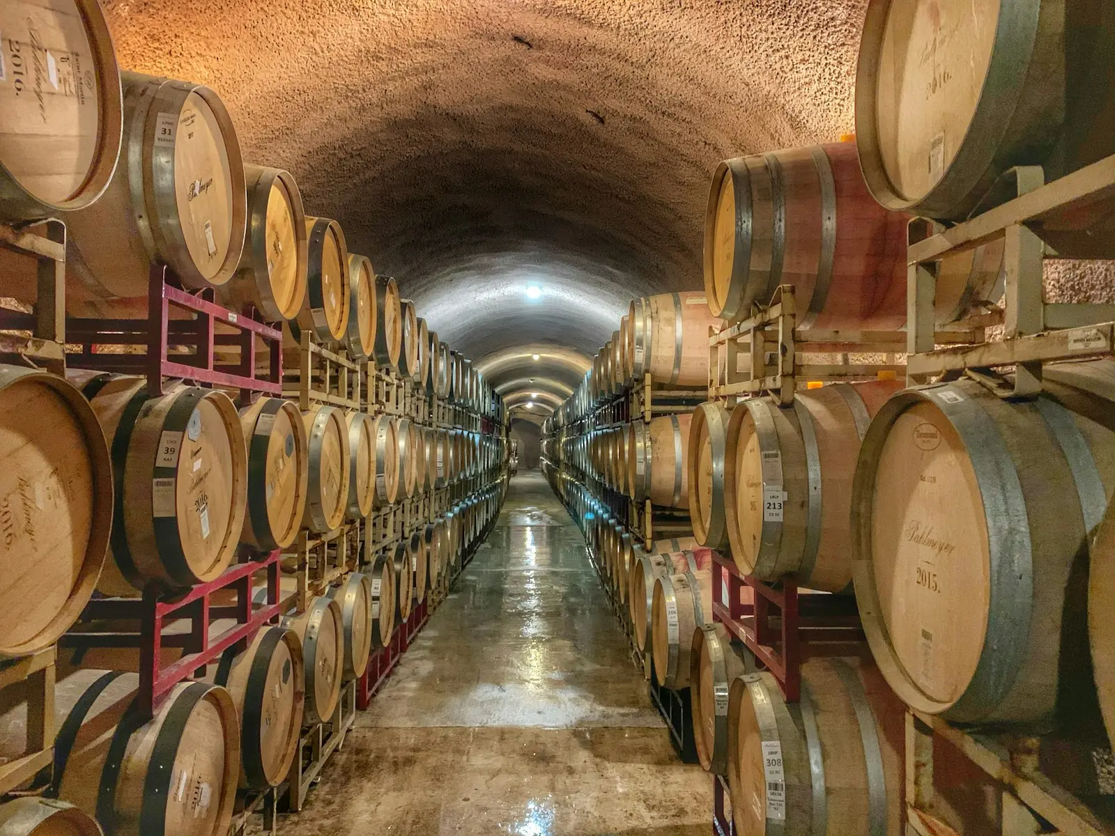 Long tunnel de cave rempli de barriques empilées, illustrant le stockage à grande échelle d'un négociant