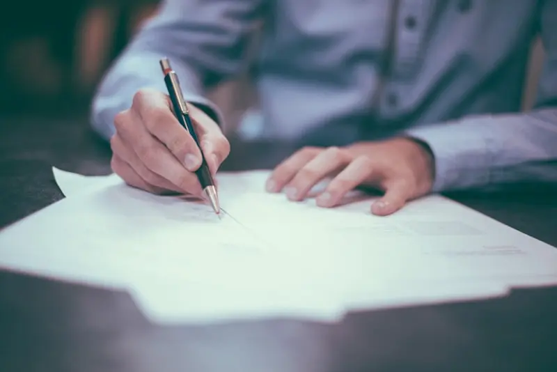 Main tenant un stylo et signant un document sur un bureau, scène de signature notariale