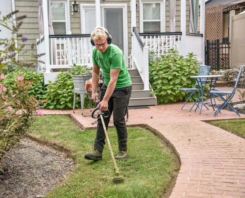 Paysagiste utilisant une débroussailleuse pour entretenir la bordure d'une pelouse