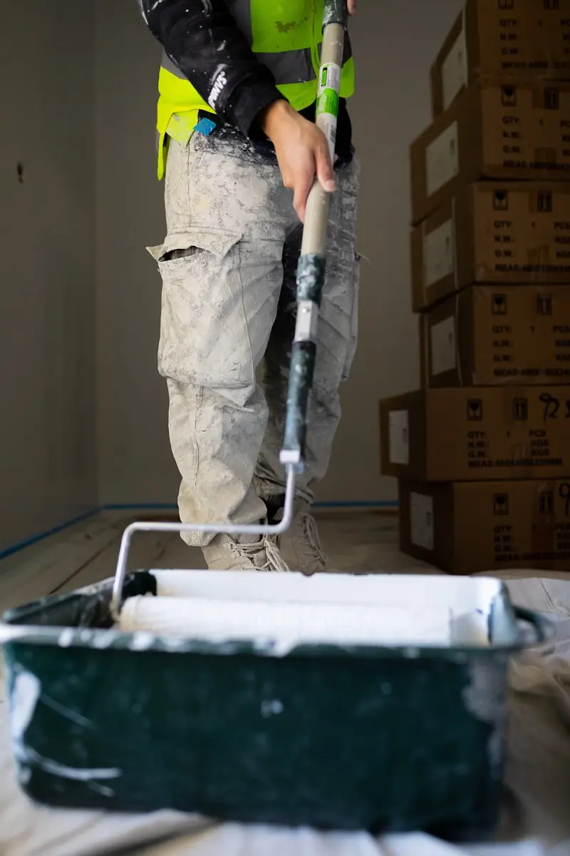 Peintre en bâtiment trempant son rouleau dans un bac de peinture blanche sur chantier