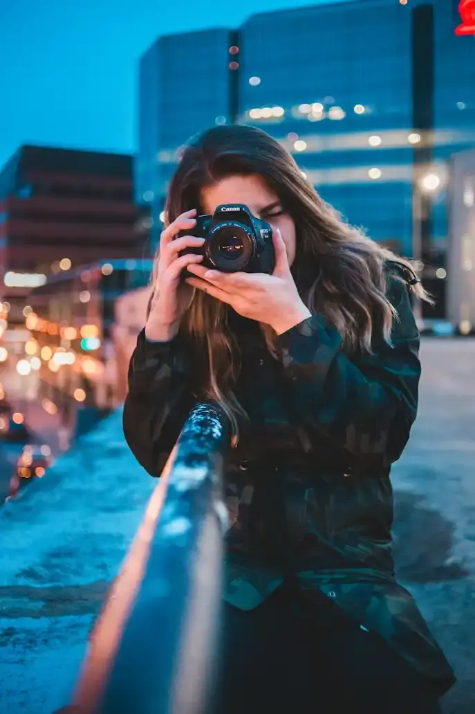 Photographe tenant un reflex Canon face à la ville illuminée à la tombée de la nuit
