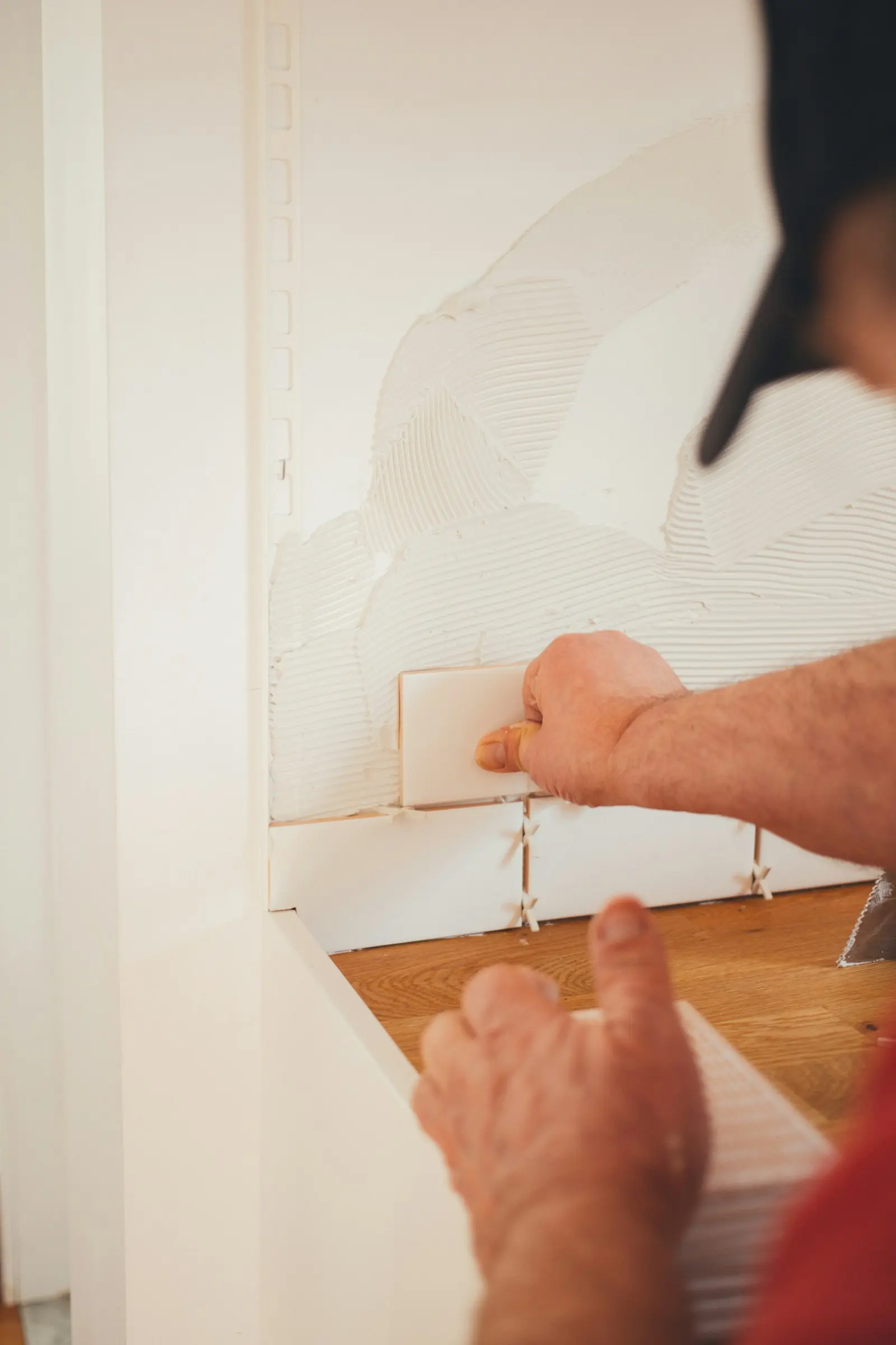Pose de carreaux muraux avec croisillons d'espacement et parquet bois en arrière-plan