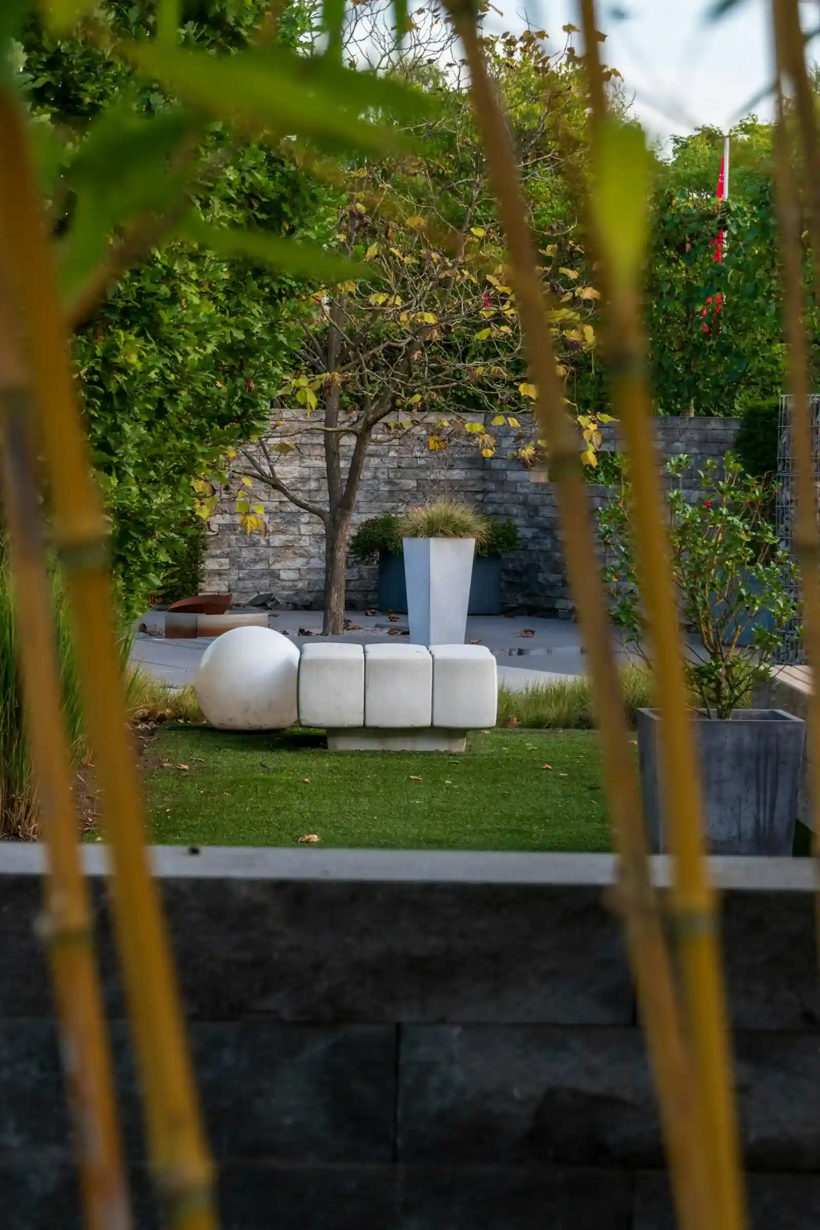Banc sculptural en béton dans un jardin paysager moderne entouré de massifs végétaux