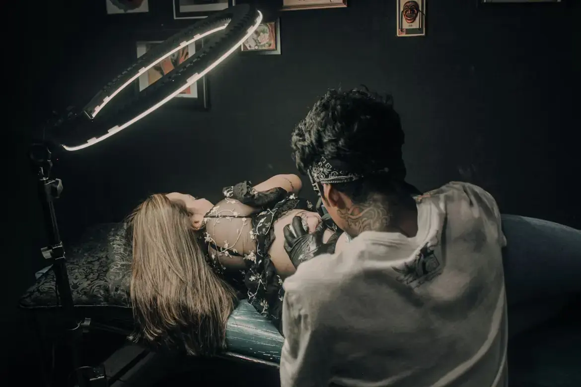 Tatoueur en plein travail sur une cliente allongée dans un studio tamisé