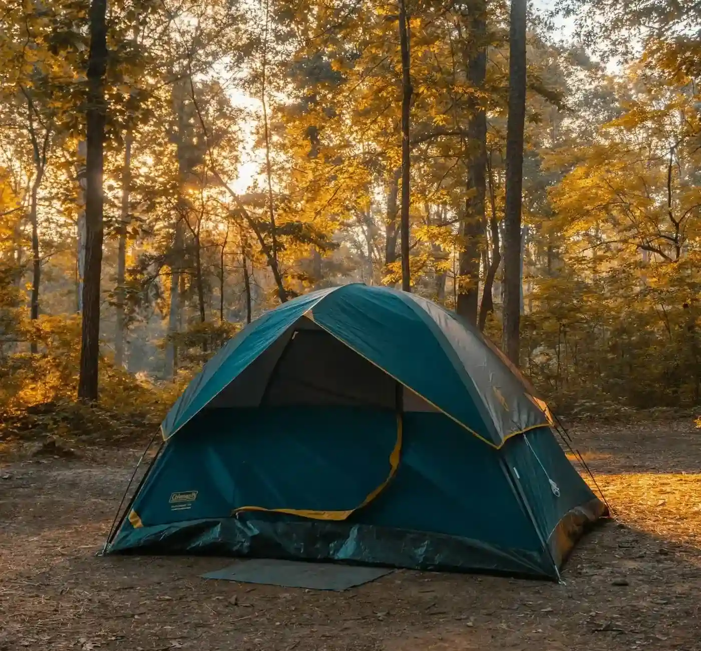 Tente de camping bleue installée dans une forêt aux couleurs automnales et lumière dorée