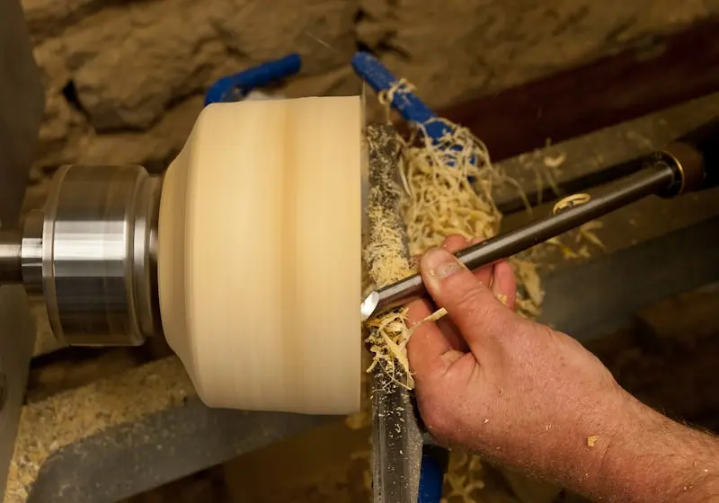 Tourneur sur bois façonnant un bol avec une gouge sur un tour, copeaux en action