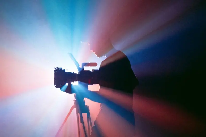 Silhouette d'un vidéaste filmant à contre-jour dans des faisceaux de lumière colorée